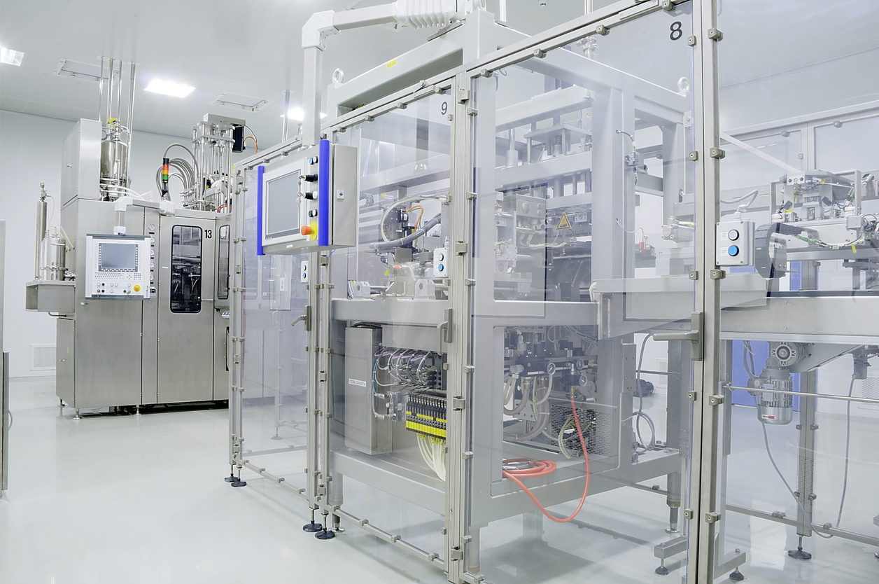 Een moderne, schone farmaceutische productiefaciliteit met geautomatiseerde roestvrijstalen machines en stelvoeten transportbanden, met bedieningspanelen in glas, die werken in een heldere, steriele omgeving.